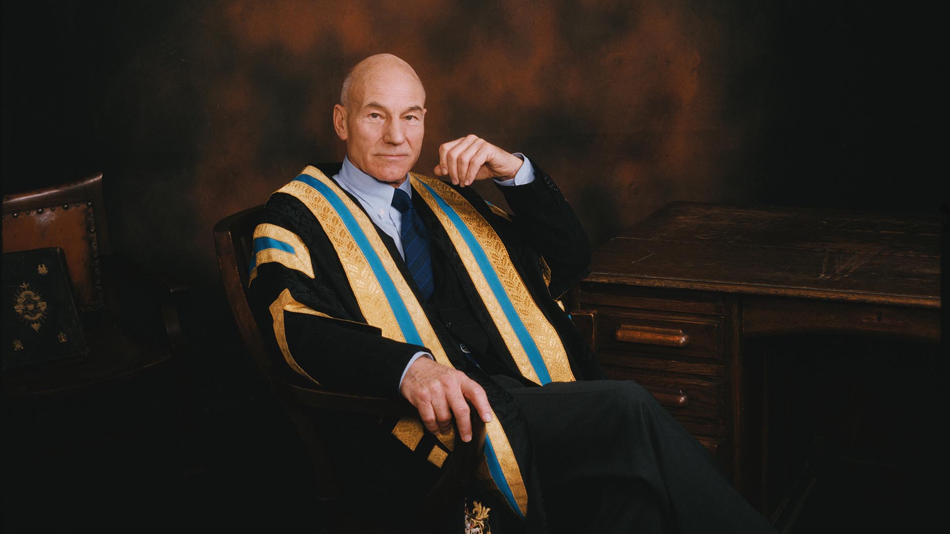 Sir Patrick Stewart looks at the camera while sat down in university robes
