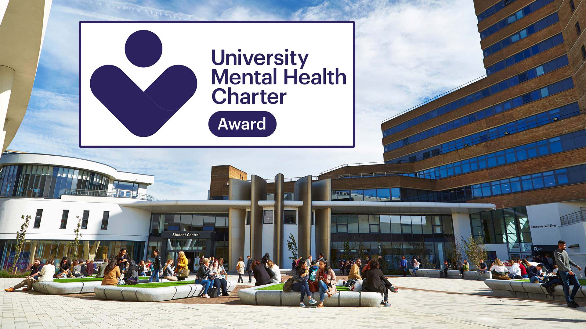 Students sat outside the University of Huddersfield main plaza with a graphic showing the University Mental Health Charter Award logo