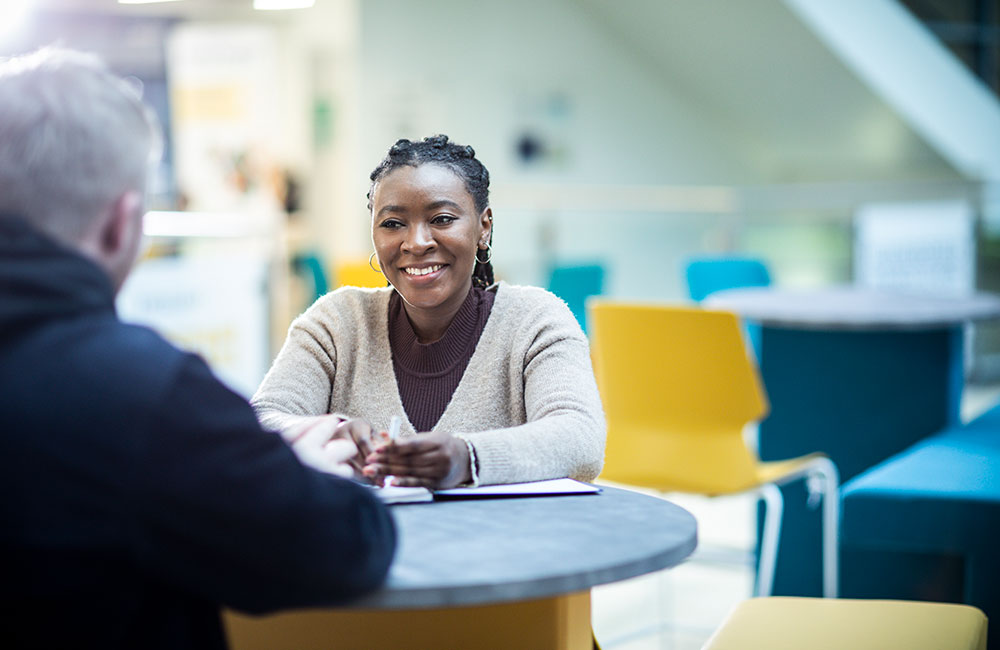 A smiling student sat at a table, with an adult sat opposite to them.