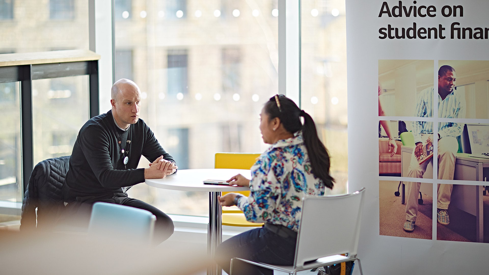 A student sat with a member of staff, there is a banner that says 'advice on student finance'' next to them.