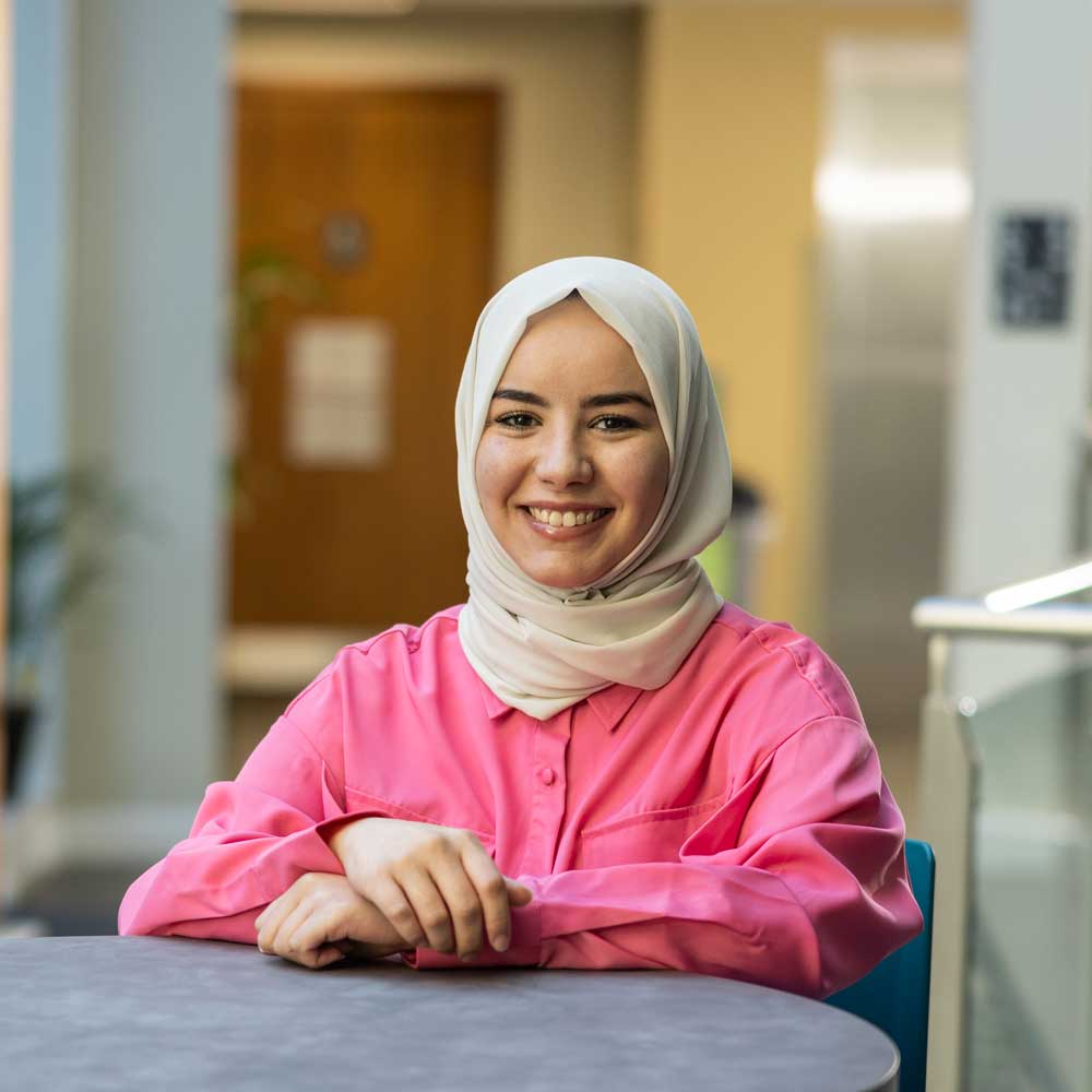 a photo of hadil sat at a table wearing pink