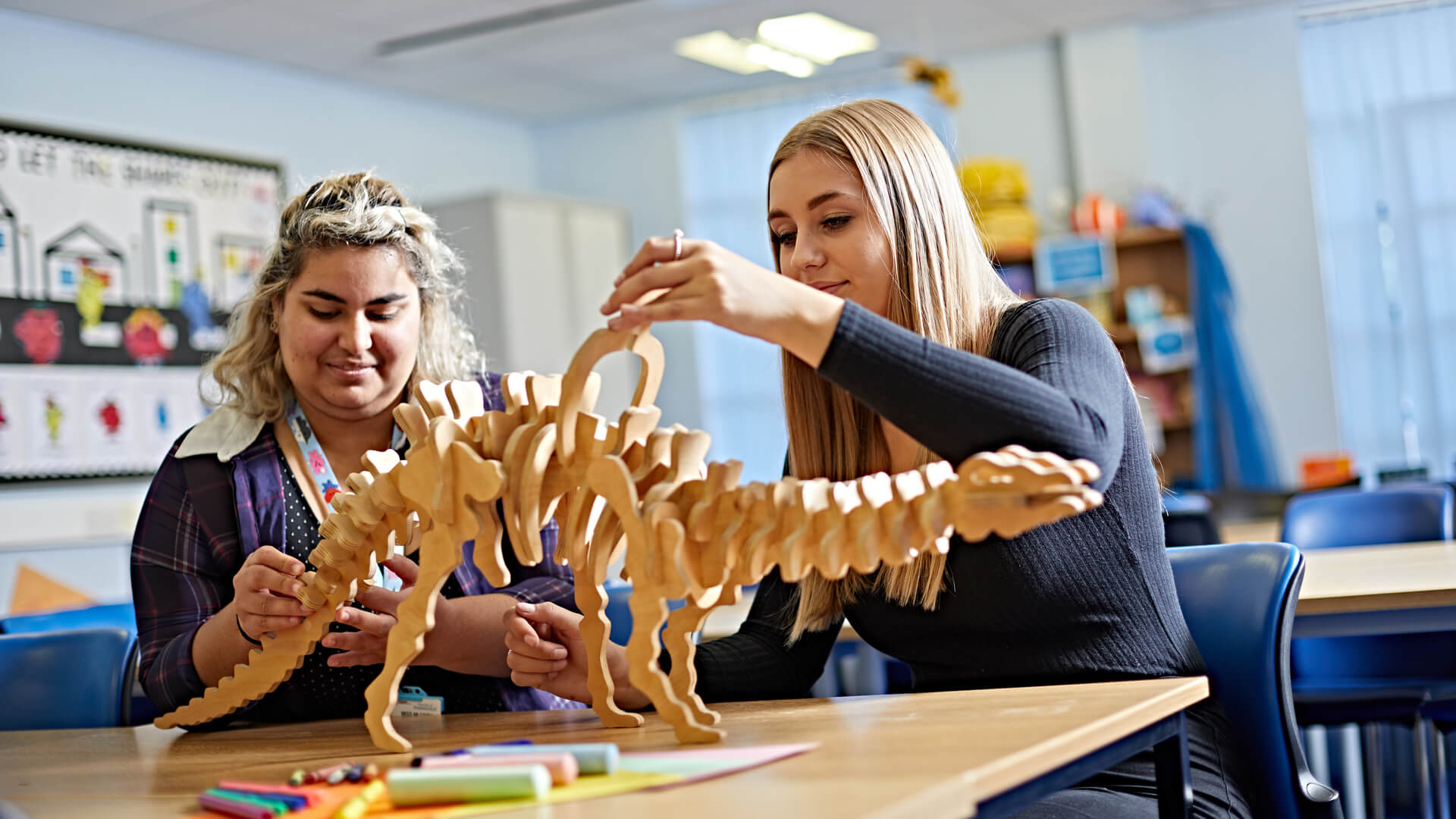 Two students sat at a table whilst constructing a wooden model of a dinosaur skeleton