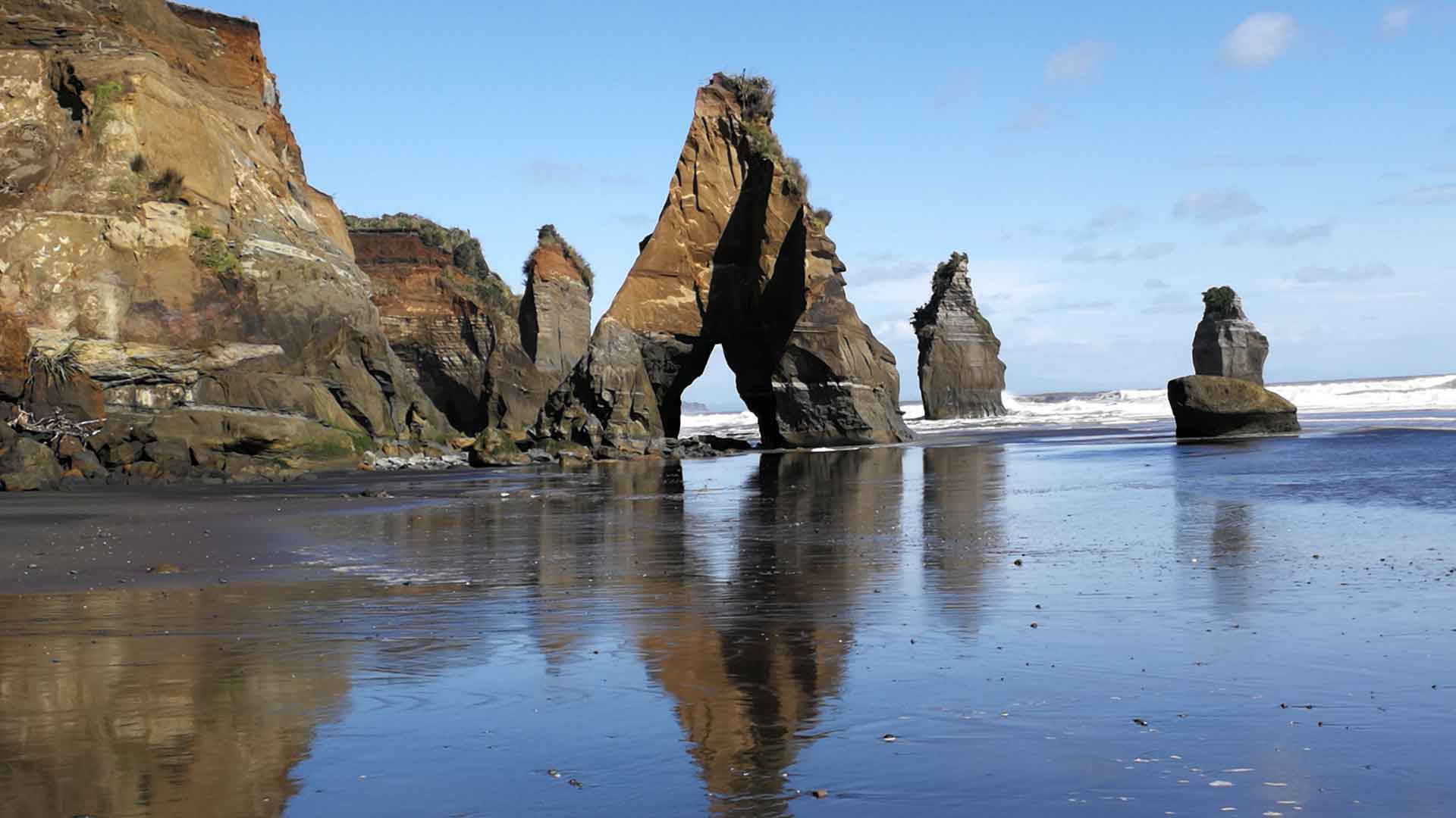 Natural arches and sea stacks reveal stratigraphy at Tongaporutu, New Zealand.Black sand beach with rock arch and sea stacks showing changes in rock type between base and top